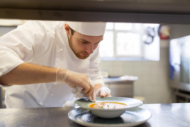 voedsel koken, beroep en mensen concept - gelukkige mannelijke chef-kok die bord soep serveert in de keuken van het restaurant