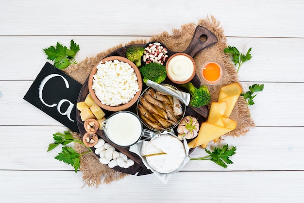 Voedsel met calcium Een verscheidenheid aan voedingsmiddelen die rijk zijn aan calcium kaas melk Parmezaanse kaas zure room vis amandelen peterselie knoflook broccoli Op een witte houten achtergrond Bovenaanzicht Gratis kopieerruimte