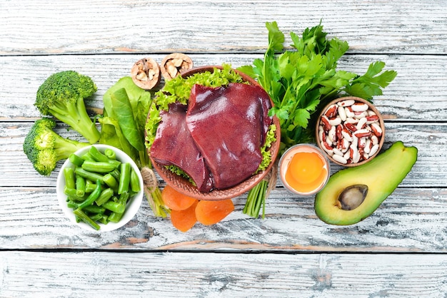 Foto voedsel met natuurlijk ijzer fe lever avocado broccoli spinazie peterselie bonen noten op een witte houten achtergrond bovenaanzicht