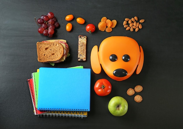 Voedsel voor schoolkind met lunchbox en notitieboekjes op donkere achtergrond