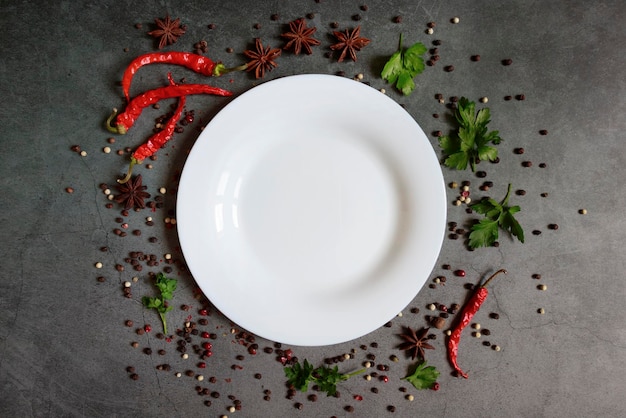 Voedselachtergrond Een lege plaat met ruimte voor tekst tussen kruiden en specerijen Chili peper piment steranijs en greens op een donkere achtergrond