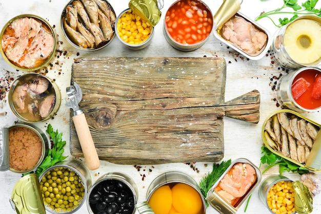 Voedselachtergrond in blikjes Ingeblikte groenten, bonen, vis en fruit op een witte houten achtergrond Bovenaanzicht