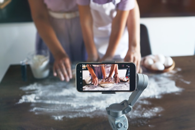 Voedselblogger moeder en dochter bereiden het deeg voor, bakken koekjes, nemen video op camera op, genieten. in de keuken.