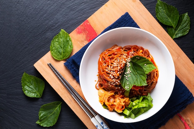 Voedselconcept koreaanse pittige koude boekweitnoedel kimchi bibim guksu op een houten bord en zwarte achtergrond met kopieerruimte