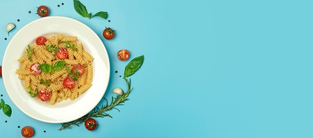Voedseldeegwaren op een blauwe achtergrond. Italiaanse fusilli pasta met tomaten, kruiden en basilicum op een witte plaat.