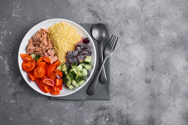 Voedseldieet concept tonijnsalade couscoussalade met geconserveerde tonijntomaten, komkommers en paarse uien op tafel kopieer ruimte