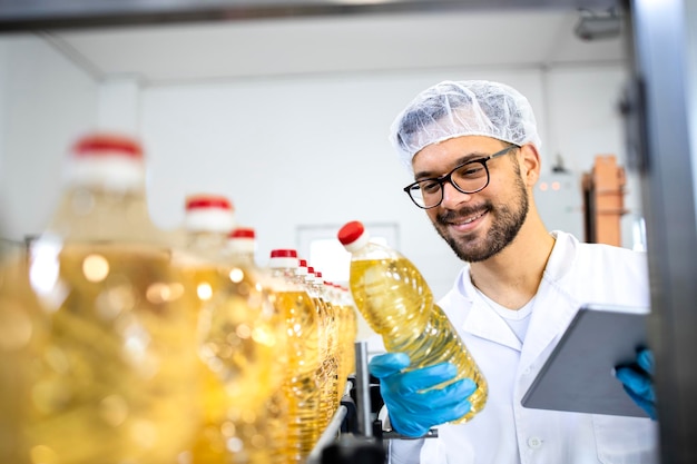 Voedselfabrieksarbeider staat bij de productiemachine en controleert de kwaliteit van de productie van plantaardige olie