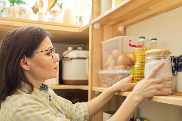 Foto voedselopslag, houten plank in bijkeuken met producten. vrouw die voedsel neemt, zonnebloemolie om te koken.