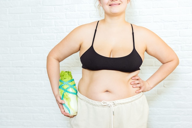 Voedselverslaving, voeding, gezondheidszorg, voedingswaarde, afvallen, gezonde voeding, welzijn. Jonge onherkenbare vrouw met overgewicht met kool in de buurt van haar zwaarlijvige buik, bijgesneden portret