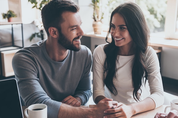 Voel me nu gelukkig. Gelukkig jong liefdevol paar hand in hand en kijken elkaar aan terwijl ze aan het bureau zitten met een man die voor hen zit