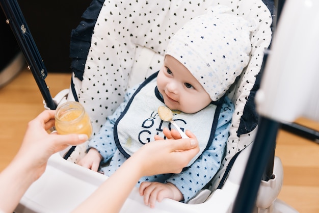 Voeren. Aanbiddelijk babykind dat met een lepel als hoge voorzitter eet. Baby