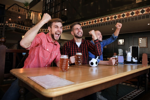 Voetbal kijken in de bar. gelukkige vrienden die bier drinken en juichen voor het favoriete team, de overwinning vieren.