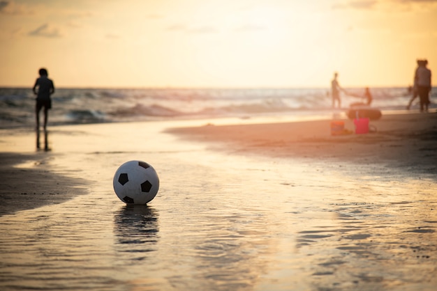 Voetbalbal op zand / speelvoetbal bij het overzees van de strandzonsondergang