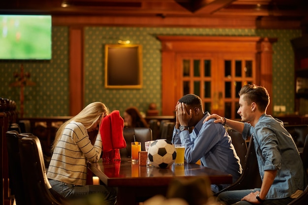 Voetbalfans met rode sjaal kijken naar spelvertaling, vrienden in de bar. Groep mensen ontspannen in pub, nachtlevensstijl, vriendschap, sportviering