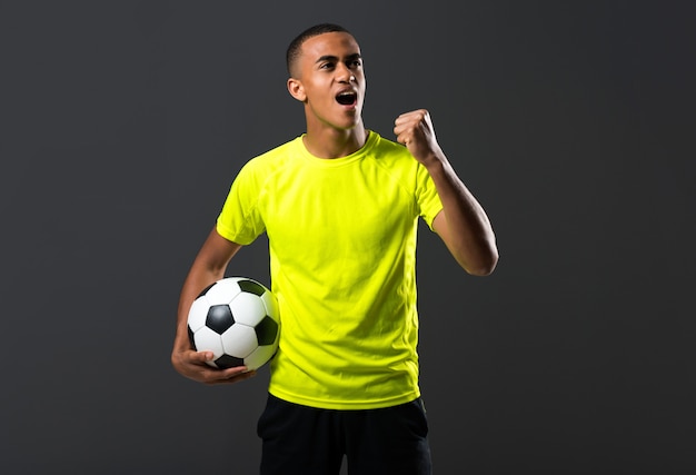 Voetballende man met donkere huidspel vangen van een bal met zijn handen op een donkere achtergrond