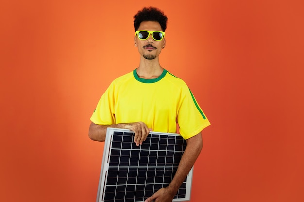 Voetballer Black Man vieren met fotovoltaïsch zonnepaneel geïsoleerd op oranje achtergrond
