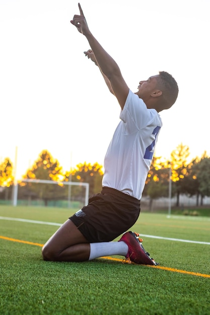 Voetballer op zijn knieën die een doelpunt viert Opgewonden voetballer die een doelpunt viert