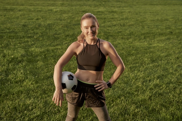 Voetbalster mooie gelukkige vrouw die voetbal vasthoudt en naar de camera glimlacht terwijl ze staat