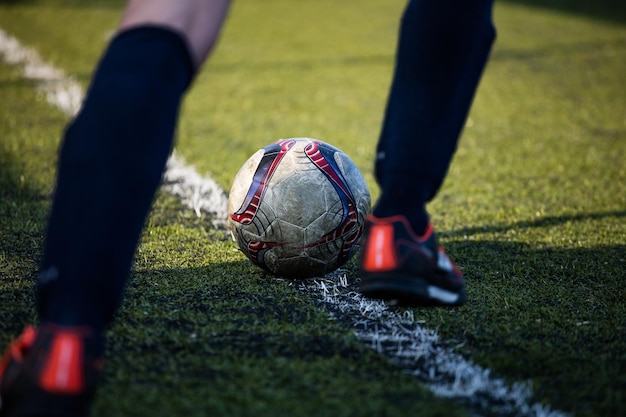 Voetbalvoetballer klaar om de voetbalbal in groen veld te trappen op een zonnige dag