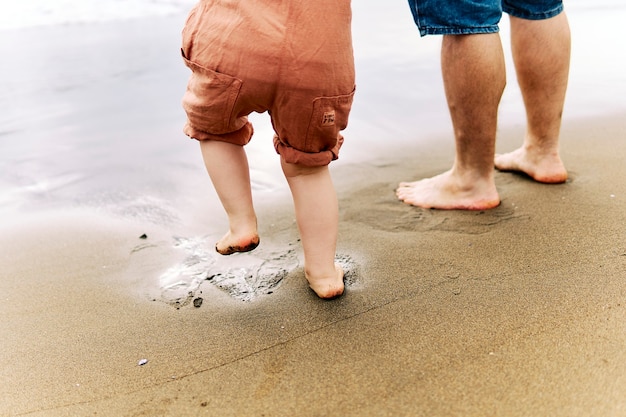 Voeten van een driejarige jongen naast zijn vader aan de kust