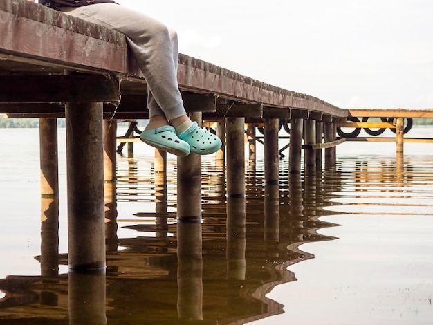 Voeten van een man zittend op een brug bij de rivier Het concept van recreatie