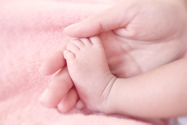 Voeten van een pasgeboren baby op witte deken in de handen van ouders, moeder en haar kind