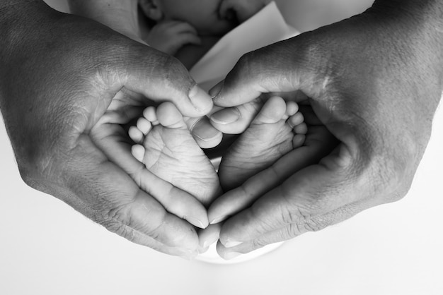 Foto voeten van een pasgeborene in de handen van mama en papa voeten van een kleine pasgeborene op ouderlijke hartvormige handen close-up benen, tenen, voeten en hielen van pasgeboren zwart-wit macro studiofoto