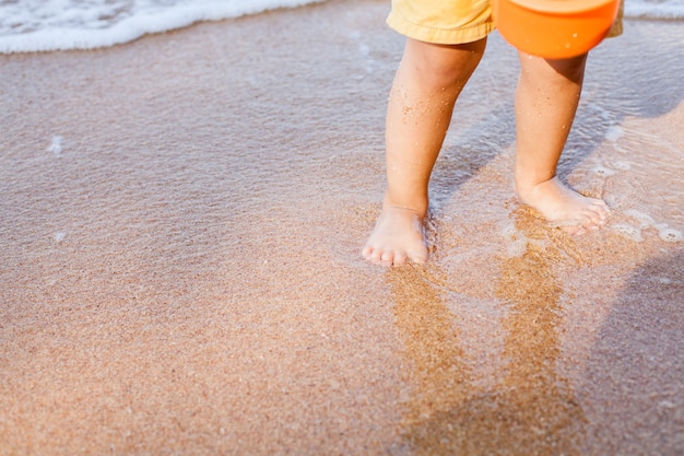 Voeten van kleine kindjongen wat betreft water en status op het strand