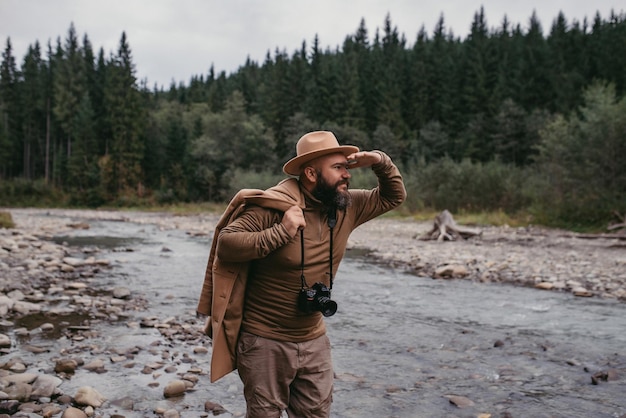 Voetganger die op de rotsen van de rivier staat met een professionele camera in zijn handen