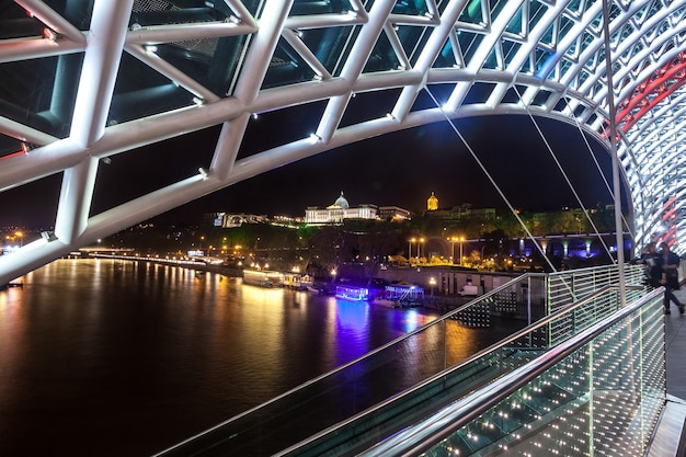 Voetgangersbrug van vrede over de Mtkvari-rivier in Tbilisi 's nachts. Georgische vlag.