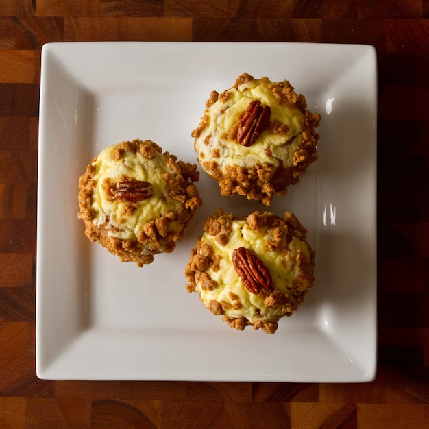 Vogelperspectief van drie oranje muffins gegarneerd met glazuur en een pecannoot op een witte plaat op een tabl