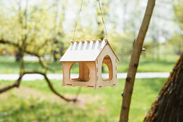 Vogelvoederhuis in de vorm van een huisje dat aan een boom hangt. Park zonnige zomerdag. Close-up van een klein houten vogelhuisje.