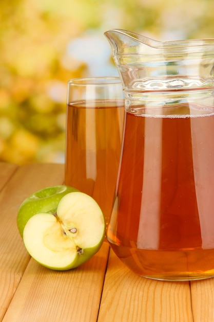 Foto vol glas en kruik appelsap en appels op houten tafel buiten