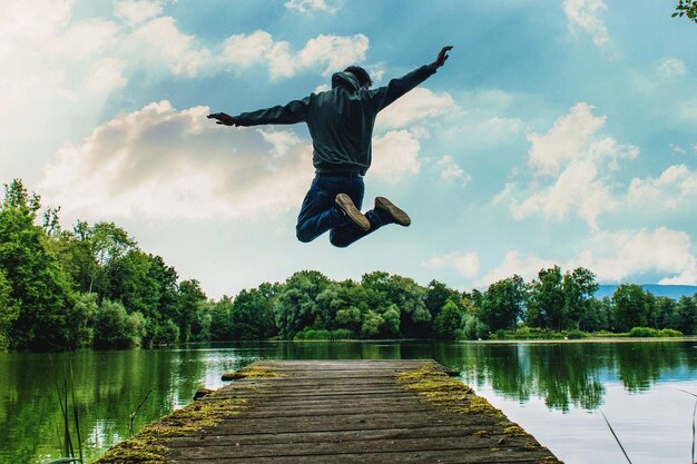 Foto vol lengte van de man springen op de pier over het meer tegen de lucht
