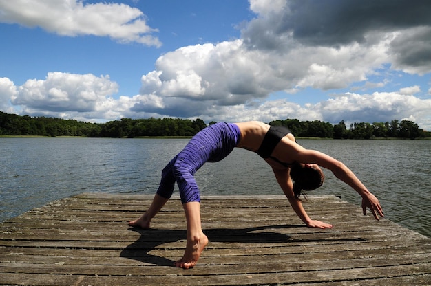 Foto vol lengte van jonge vrouw die yoga doet op de steiger bij het meer
