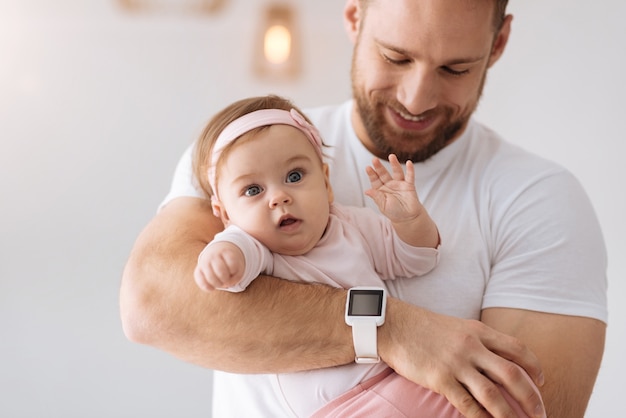 Vol nieuwsgierigheid. mooie vrij betrokken baby die in de handen van de jonge vader ligt en wegkijkt terwijl hij interesse en positiviteit uit