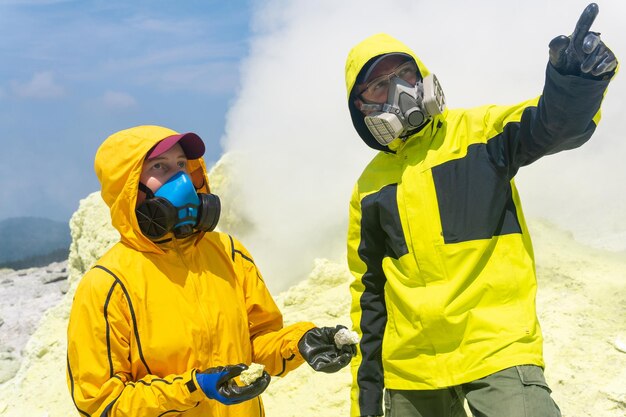 Volcanologists on the slope of the volcano collect samples against the backdrop of smoking sulfur fumaroles