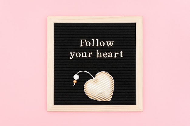Volg je hart. Motiverend citaat in gouden letters en decoratief textielhart op zwart brievenbord