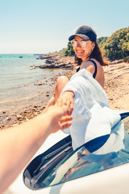 Volg mij concept vrouw zittend op de motorkap van de auto rustend op het strand