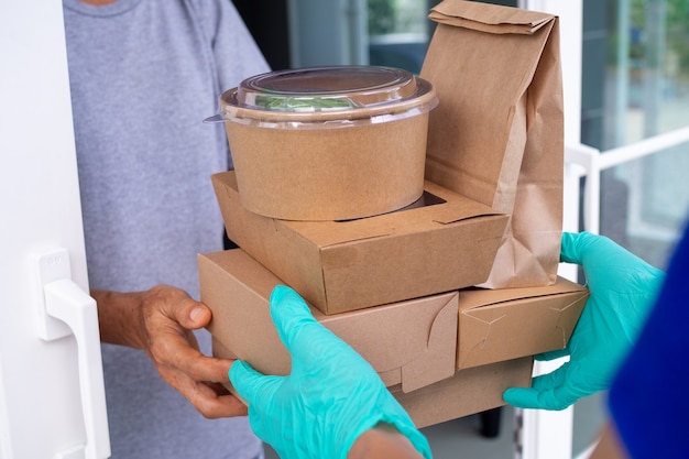 Volgens het bevel stuurt een gehandschoende medewerker voedseldozen naar klanten voor de deur. Concept van levering, online levering