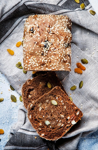 Volkoren biologisch rogge donker brood met pompoenpitten, gedroogde vruchten, rozijnen en sesamzaadjes op grijze handdoek op de keukentafel achtergrond bovenaanzicht ruimte voor verticale tekstafbeelding