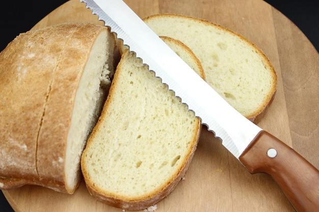 Volkoren brood op een houten keukenbord met een koksmes om op zwarte achtergrond te snijden