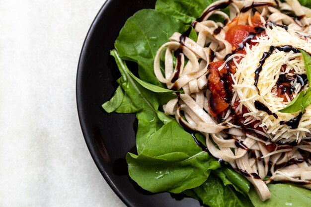 Volkoren pasta pasta met Parmezaanse kaas, groene bladeren van rucola, rode saus en balsamico azijn op zwarte plaat en witte marmeren achtergrond