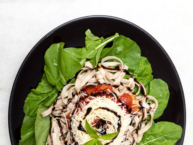 Volkoren pasta pasta met Parmezaanse kaas, groene bladeren van rucola, rode saus en balsamico azijn op zwarte plaat en witte marmeren achtergrond