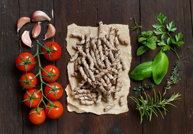 Volkoren pasta, tomaten, knoflook en kruiden op een houten ondergrond