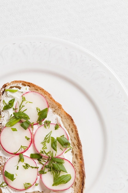 Volkoren sandwich met biologische radijs en roomkaas op witte plaat en strotafelmat