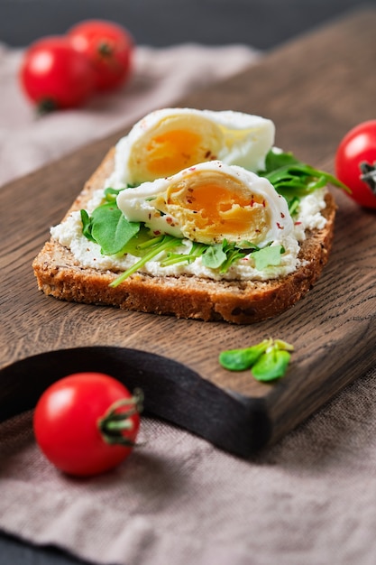 Volkoren sandwiches met guacamole, tomaat, rucola en ei. Ontbijt op een houten bord.