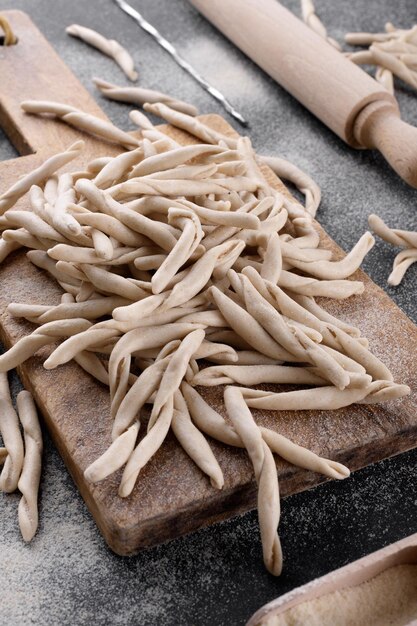 Volkoren tarwe Apulische pasta genaamd Pizzarieddi of maccaruni op een snijplank op zwarte tafel. Verse maccheroni typische schotel van Puglia, Salento Italië. Italiaanse zelfgemaakte pasta achtergrond, close-up