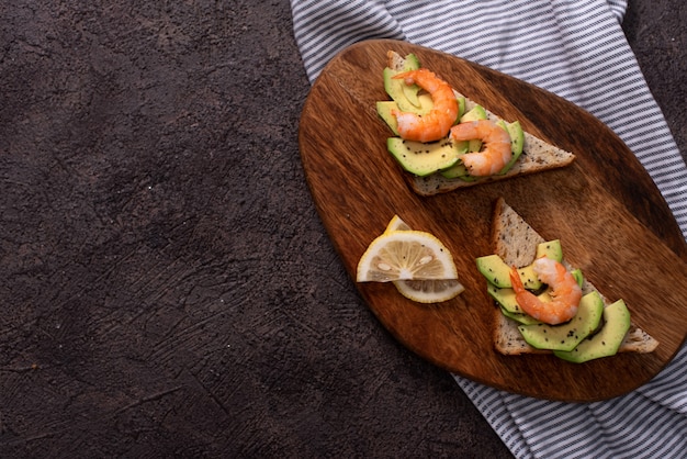 Foto volkoren toast sneetjes brood met guacamole, gebakken garnalen en stukjes gebakken spek op houten plank selectieve aandacht, focus op de voorkant van de garnalen op het eerste brood