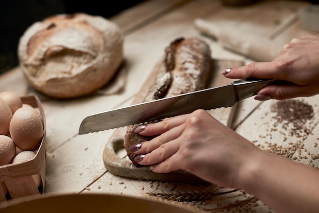 Volkorenbrood op keukenhoutplaat met een chef-kok die een gouden mes vasthoudt om te snijden